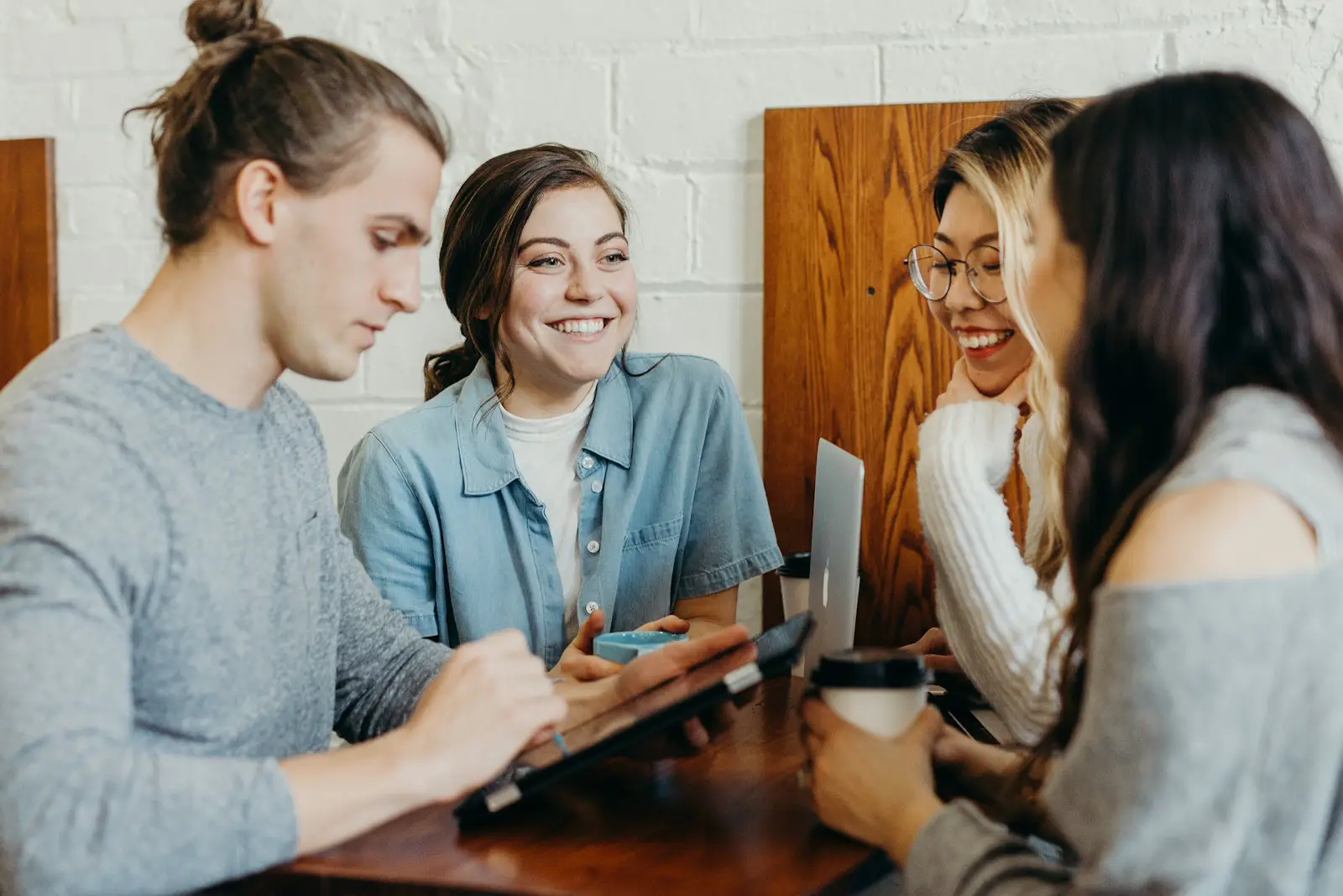 Four friends around a café table, two of them laughing, with coffee cups and a tablet between them