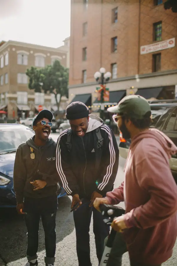 Three friends laughing together on a city pavement on an overcast day